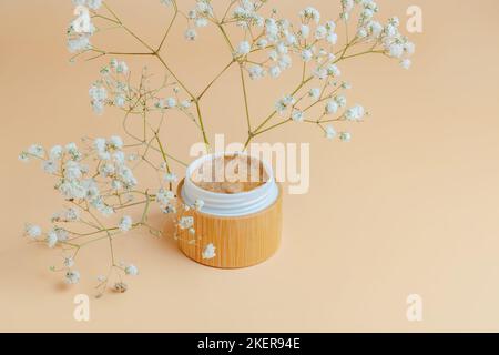 Scrub naturale su sfondo beige. Contenitore di bambù per la crema viso cosmetica con prodotti non crudeltà. Modello per barattolo di scrub con zucchero per il caffè del corpo Foto Stock