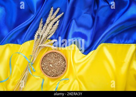 Spikelets di grano e ciotola con grani di grano sullo sfondo della bandiera dell'Ucraina. Raccolto di grano e concetto di Ucraina Foto Stock