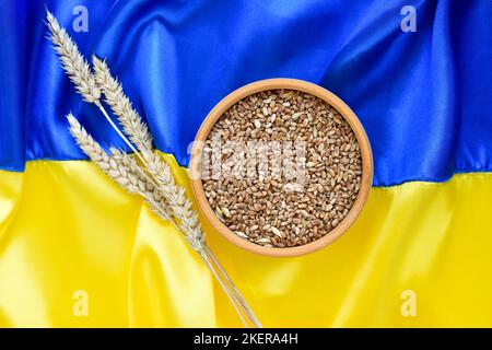 Spikelets di grano e ciotola con grani di grano sullo sfondo della bandiera dell'Ucraina. Raccolto di grano e concetto di Ucraina Foto Stock