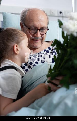 Bambina che dà fiori bouquet presente, nonno abbraccio ricoverato in ospedale. Paziente anziano che dice Arrivederci bambino piccolo in clinica geriatrica visita stanza. Foto Stock