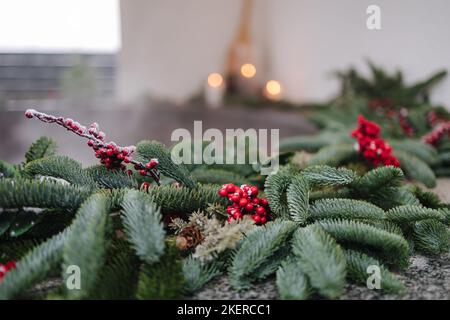 Macro foto della vasca calda in ghisa fumante con idromassaggio in inverno con neve e candele decorate. Rametti di Natale con rosa guelder e coni di pino Foto Stock