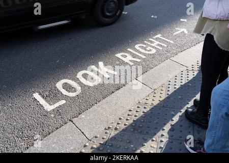 L'iconica segnaletica stradale dipinta "Look Right" per i pedoni di Londra con un passaggio in auto. Concetto: Attraversamento della strada, sicurezza stradale, pedoni in attesa Foto Stock