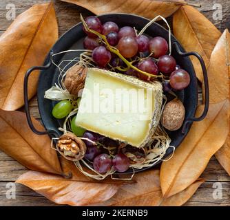 fetta di pecorino con fieno di montagna, su sfondo autunnale con uve nere Foto Stock