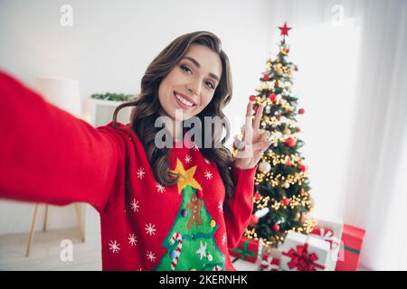 Primo piano selfie foto cadre di giovane soddisfatto blogger mostrando segno v toothy beaming sorriso prendere scatto della sua atmosfera di casa natale al coperto Foto Stock