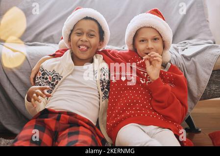 Felici ragazzi interrazziali che indossano costumi festosi, cappelli di Babbo Natale, leccare canne caramelle, divertirsi Foto Stock