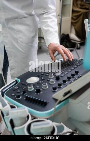 vista ritagliata del medico in bianco camice regolazione ecografo in clinica, immagine stock Foto Stock