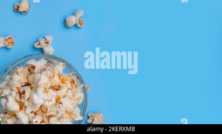 Delizioso popcorn in ciotola di vetro su sfondo blu pastello. Vista dall'alto del popcorn caldo con spazio per fotocopie, snack cinematografici e intrattenimento. Foto Stock