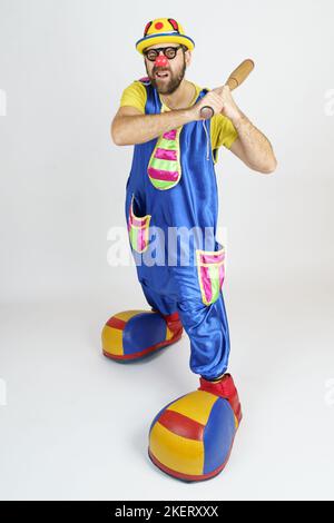 Concetto di vacanza. Il clown è un uomo in un vestito blu e giallo brillante con una mazza da baseball. Foto Stock