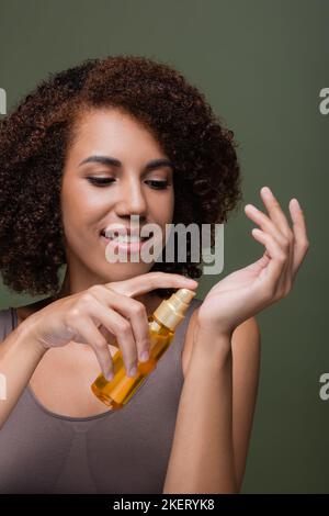 Donna afro-americana positiva che applica l'olio cosmetic sulla mano isolato su verde, immagine di riserva Foto Stock