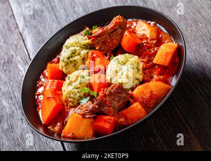 Stufato di manzo con gnocchi e verdure in ricco pomodoro e sugo a base di brodo in ciotola nera, primo piano Foto Stock