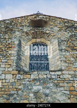 Una piccola finestra con una vetrata in una vecchia chiesa in pietra Foto Stock