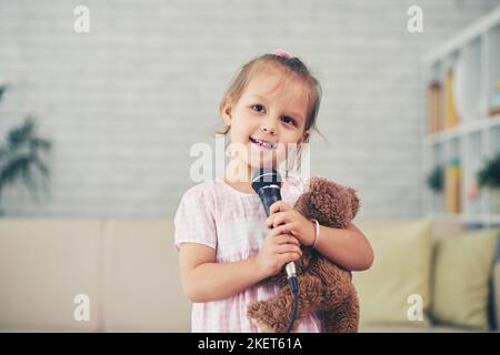 Ritratto di una bambina sorridente che canta una canzone nel microfono Foto Stock