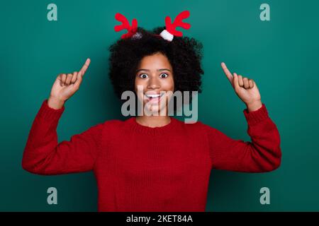 Ritratto fotografico di affascinante bambina eccitato punto nuovo anno corna cervi indossare abiti a maglia rosso trendy isolato su sfondo di colore verde Foto Stock