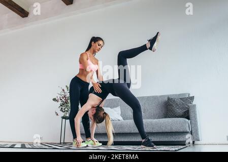 Adatta la donna che fa arcate indietro con l'aiuto di personal trainer supportandola Foto Stock