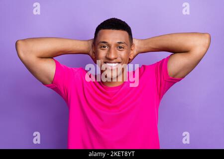 Foto di rilassato positivo piacevole scatola ragazzo taglio capelli vestiti rosa t-shirt braccia dietro la testa dentale e isolato su sfondo di colore viola Foto Stock