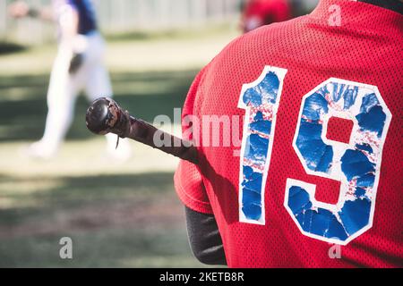 Primo piano della parte posteriore di un giocatore di baseball che tiene una mazza con il numero 19 su un'uniforme della squadra della camicia rossa Foto Stock