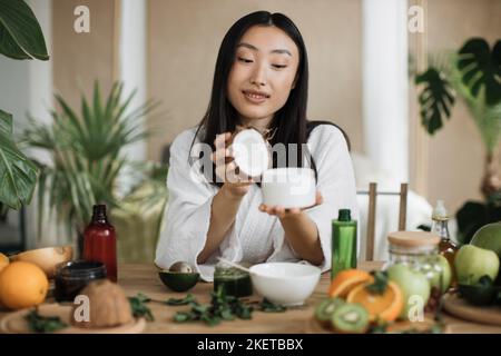 Focus su vaso di cocco e vetro, giovane donna asiatica che tiene la metà di cocco e fare crema fatta in casa Foto Stock