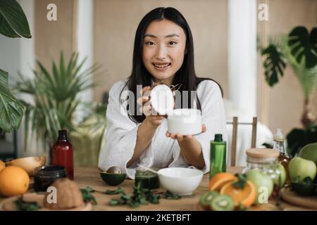 Focus su vaso di cocco e vetro, giovane donna asiatica che tiene la metà di cocco e fare crema fatta in casa Foto Stock