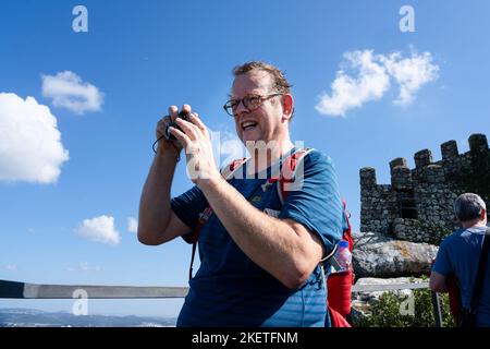 Un turista anziano sulle mura e torrette fortificate scatta foto al castello moresco dei Mori del X secolo (Castelo dos Mouros) sopra Sintra. Foto Stock