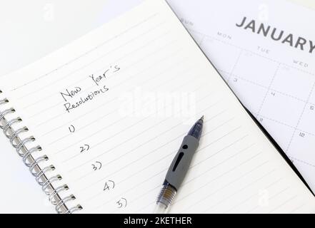 Blocco note con elenco delle risoluzioni di Capodanno scritte a mano e penna in cima al calendario di gennaio in background, focus selettivo Foto Stock
