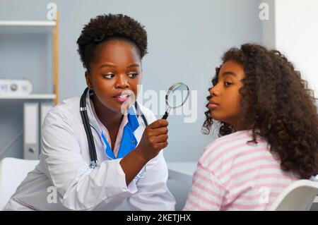 Dermatologist femminile esamina il volto della ragazza adolescente con lente d'ingrandimento per nei e rossore. Foto Stock