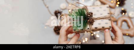 Le mani dei bambini tengono un piccolo regalo di Natale. Il concetto di dolci natalizi, giocattoli, ghirlande e bokeh. Arredamento per le vacanze di Capodanno. Foto Stock