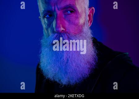 Foto di sospettoso pensionato uomo vestito nero pullover anti santa cercando spazio vuoto copyspace isolato di colore blu scuro sfondo Foto Stock