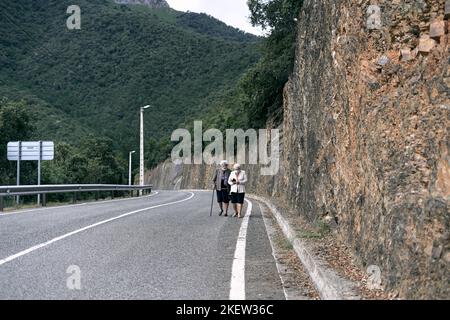 due anziane donne caucasiche con capelli bianchi e una canna in mano camminando lungo la pericolosa strada accanto al bosco con maschera facciale, ruta del cares Foto Stock
