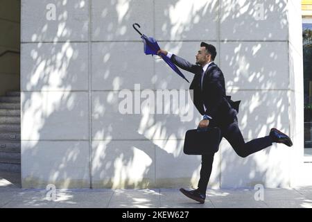 Uomo d'affari con ombrellone che corre per prendere un taxi o un autobus Foto Stock