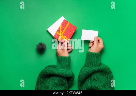 Le mani femminili tengono un kata regalo e una scatola rossa con un nastro dorato su uno sfondo verde. Concetto di Natale, Capodanno, San Valentino e compleanno Foto Stock