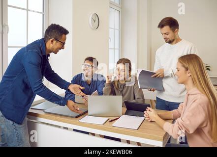 Gli studenti felici siedono alla scrivania e comunicano mentre si preparano per l'esame o studiano insieme. Foto Stock