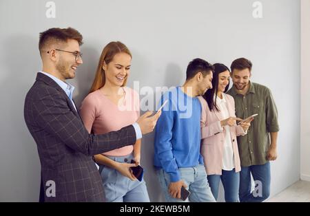 I giovani felici con i telefoni cellulari moderni si divertono a discutere le applicazioni mobili e a chattare. Foto Stock