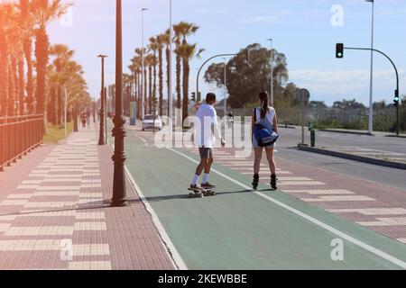 vacanze in vacanza. una donna sui pattini a rotelle e un uomo su uno skateboard si divertono all'aperto in estate giorno di sole. concetto di amore e amicizia. Alto Foto Stock