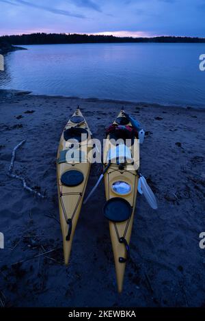 Coppia di kayak marini gialli attratti sulla spiaggia di un'isola dell'arcipelago di Stoccolma, Svezia. Visto di notte, un tramonto vago sullo sfondo. Foto Stock