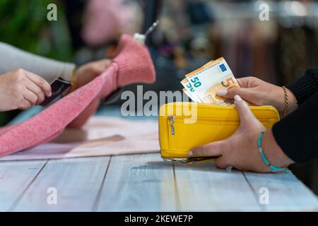 Bancone con un cliente che paga in contanti prelevando le fatture in euro dal suo portafoglio Foto Stock