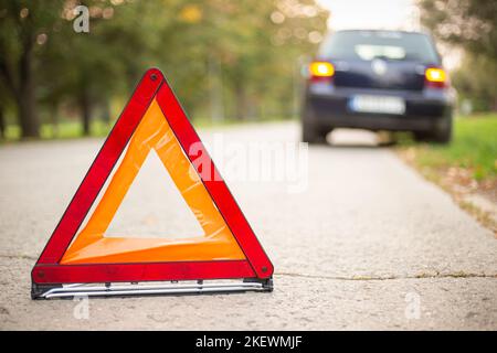 Triangolo segnaletico rosso con un'auto rotta. Triangolo di emergenza sulla strada, auto ferma. Foto Stock
