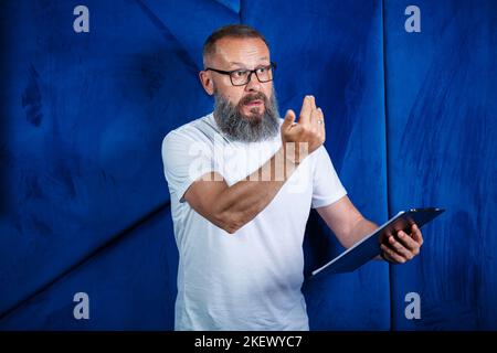 Mentore adulto maschio, direttore, uomo d'affari in occhiali e un vestito che studia documenti mentre si siede al tavolo. Concetto di giornata lavorativa Foto Stock