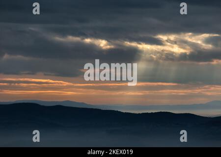 Raggi del sole che scendono da alcune nuvole sopra le montagne Foto Stock