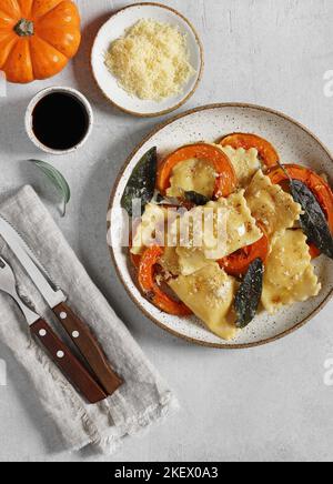 Ravioli di zucca fatti in casa con ricotta servito burro salvia , formaggio, pezzetti di zucca e posate su tovagliolo di lino . top vista verticale Foto Stock