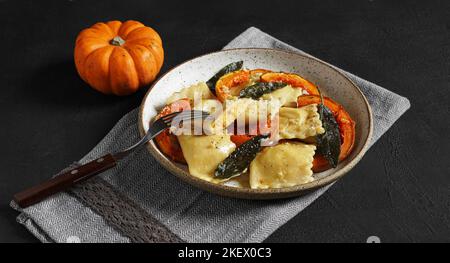 Ravioli di zucca fatti in casa con ricotta servito burro salato e formaggio duro su piatto su tavolo nero con zucca piccola. Fuoco selettivo Foto Stock