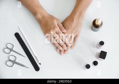 Concetto di cura delle mani. Le mani delle donne senza manicure sono sdraiate sul tavolo prima di iniziare la manicure. Mani in primo piano, gli accessori per manicure sono sdraiati accanto a lei sul tavolo. Vista dall'alto, senza una faccia. Foto Stock