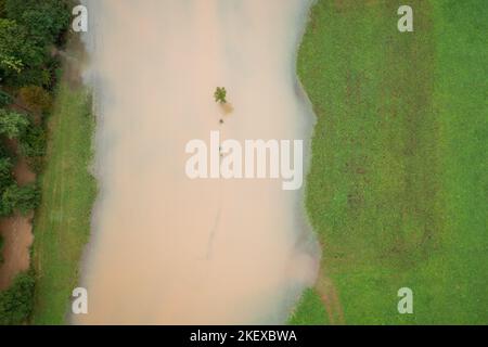Fiume sulle rive che si immergono nei campi dopo la pioggia pesante, acqua che si avvicina alle case, tiro aereo dall'alto verso il basso. Foto Stock