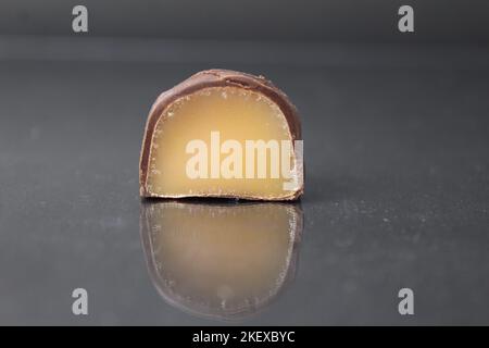 caramella al cioccolato in sezione con pralina di ripieno alla frutta marrone giallo. Caramelle di marmellata di gelatina in primo piano al cioccolato su sfondo nero. Cioccolatini Foto Stock