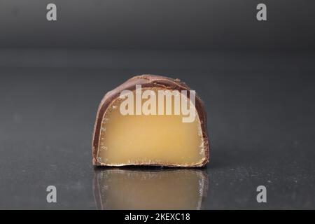 caramella al cioccolato in sezione con pralina di ripieno alla frutta marrone giallo. Caramelle di marmellata di gelatina in primo piano al cioccolato su sfondo nero. Cioccolatini Foto Stock