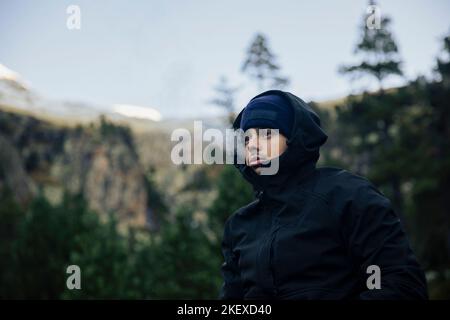 Ragazzo con cappotto e cappello che fuma una sigaretta di marijuana in natura Foto Stock