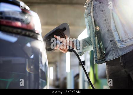 Sezione centrale dell'uomo che collega il cavo durante la ricarica dell'auto elettrica Foto Stock