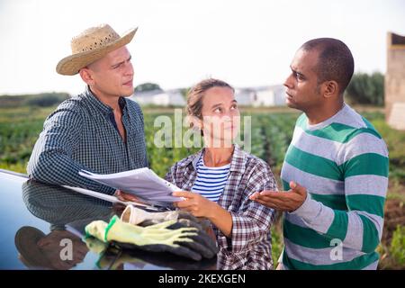 Agricoltori con documenti in piedi vicino all'auto in campo agricolo, parlando di alcune questioni attuali Foto Stock