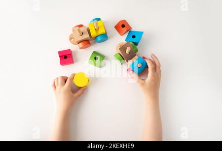 Colpo ad angolo alto di mani di un bambino e di un giocattolo di legno. Il bambino raccoglie un selezionatore. Giocattoli di logica educativa per bambini. Primo piano delle mani dei bambini. Montessori G Foto Stock