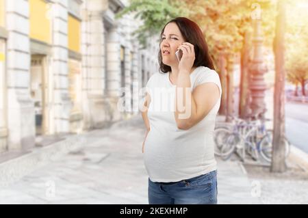 Donna incinta dolorosa che chiama assistenza medica in città Foto Stock