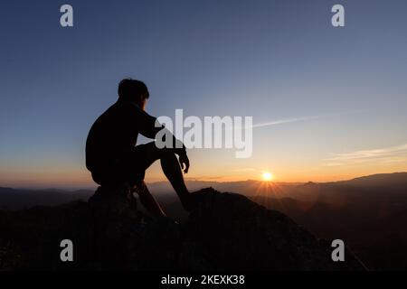 Silhouette di uomo triste seduto da solo su una montagna al tramonto, depressione e solitudine. Il concetto di stress e di culo. Foto Stock